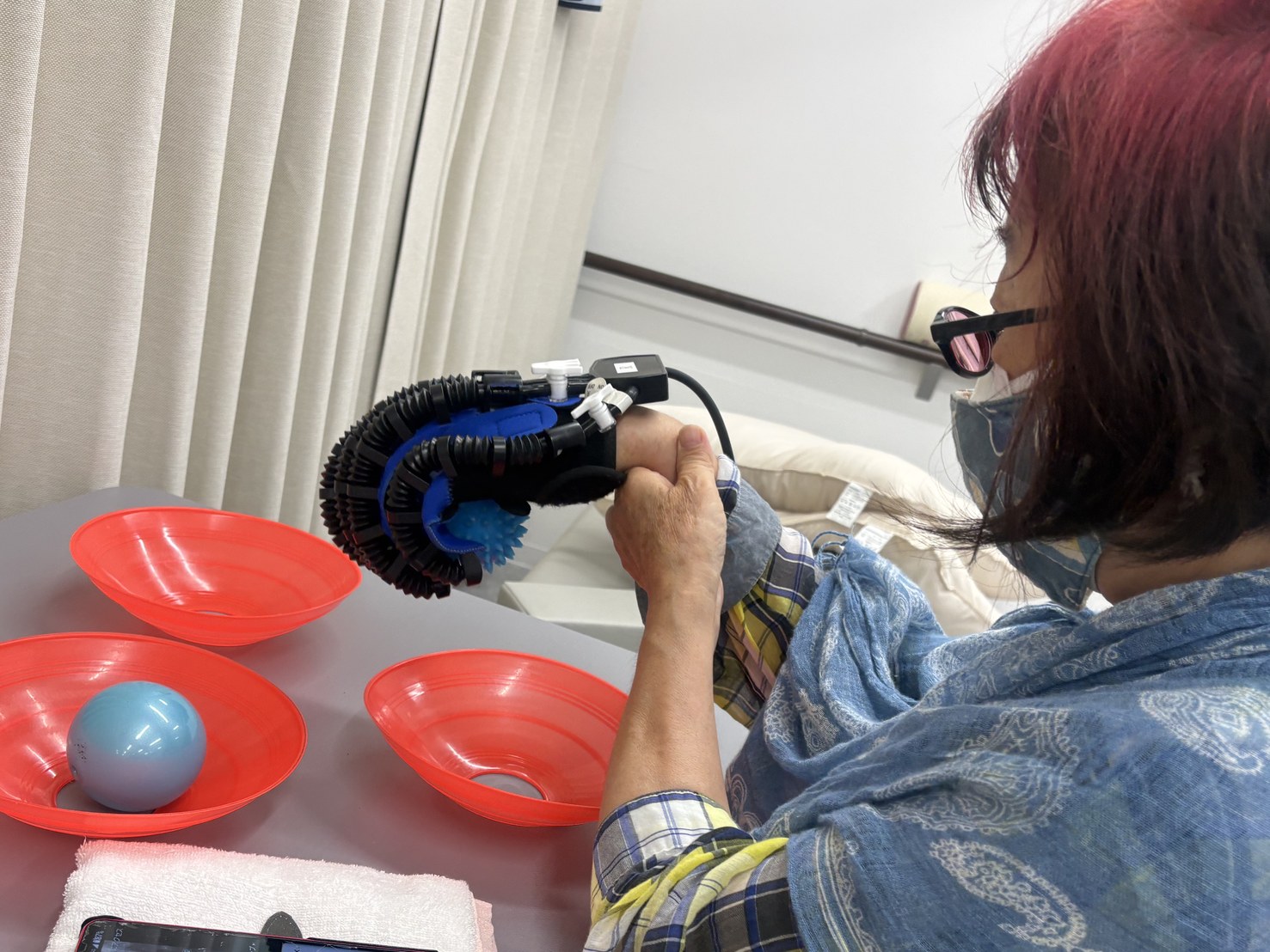 ロボットグローブを装着し、皿に置いたボールをつかんで持ち上げる手指の訓練