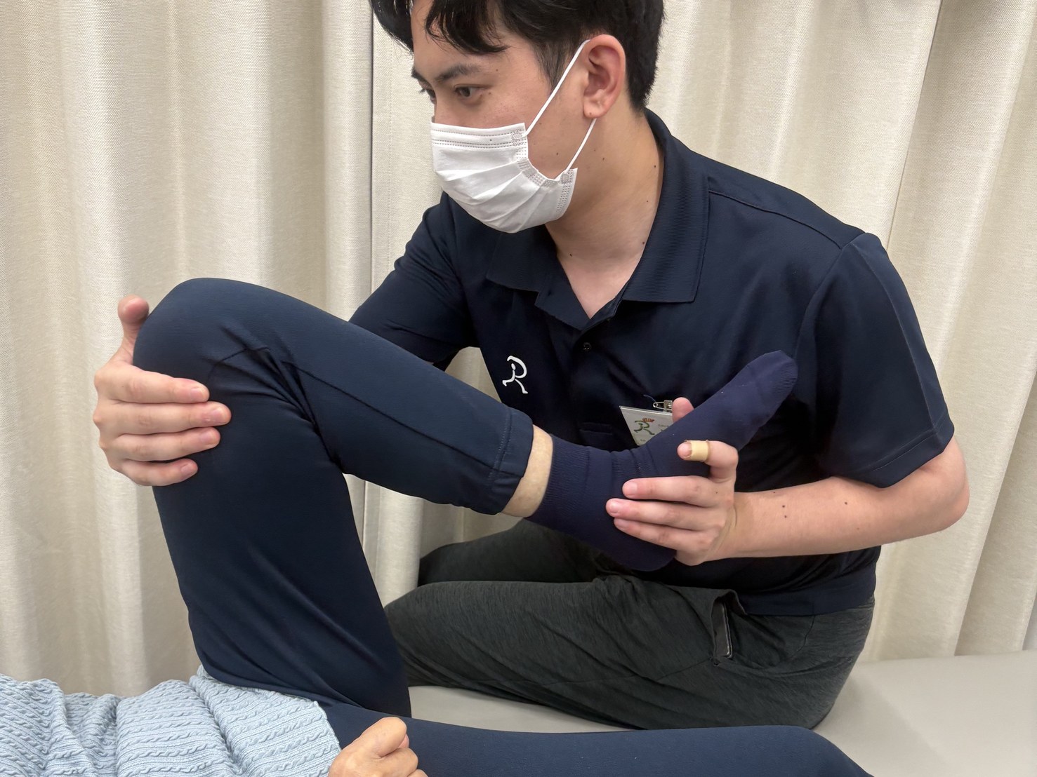 ベッドの上でスタッフが膝と足首を支え、下肢の関節をゆっくり動かす訓練